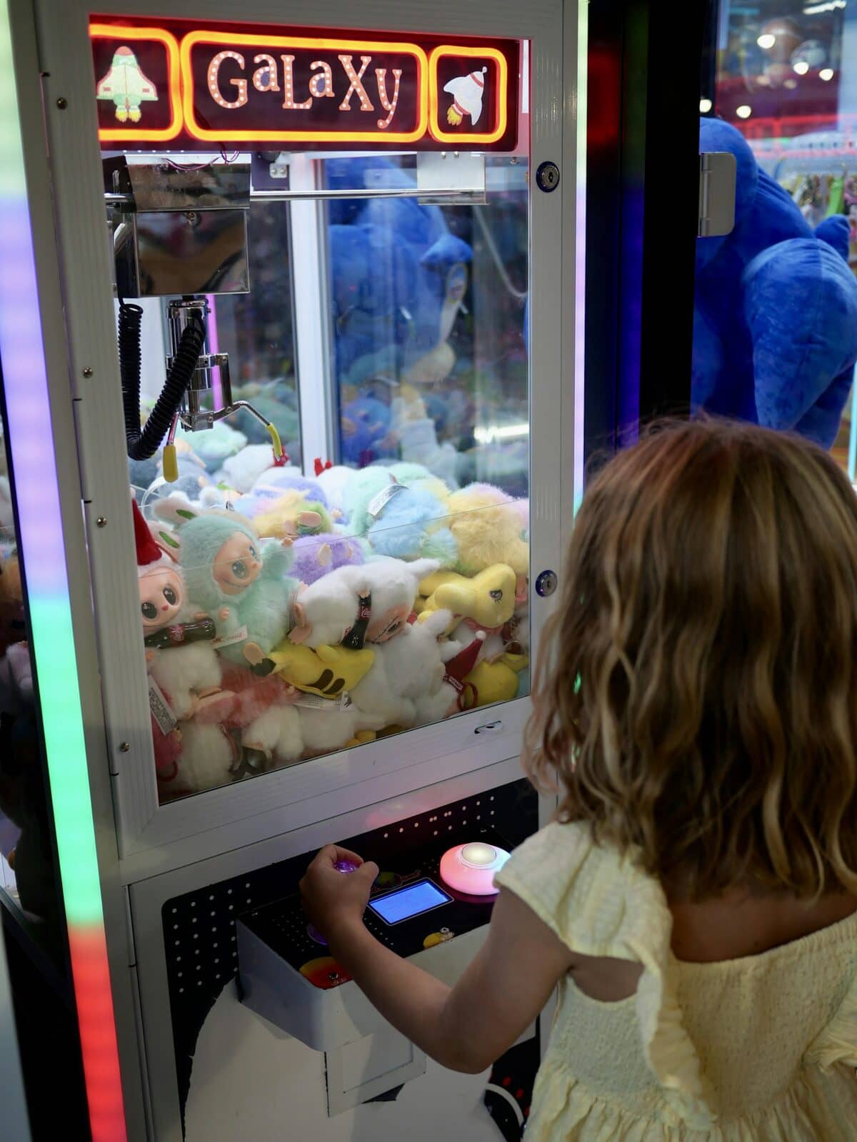 A girl playing a brightly lit claw machine